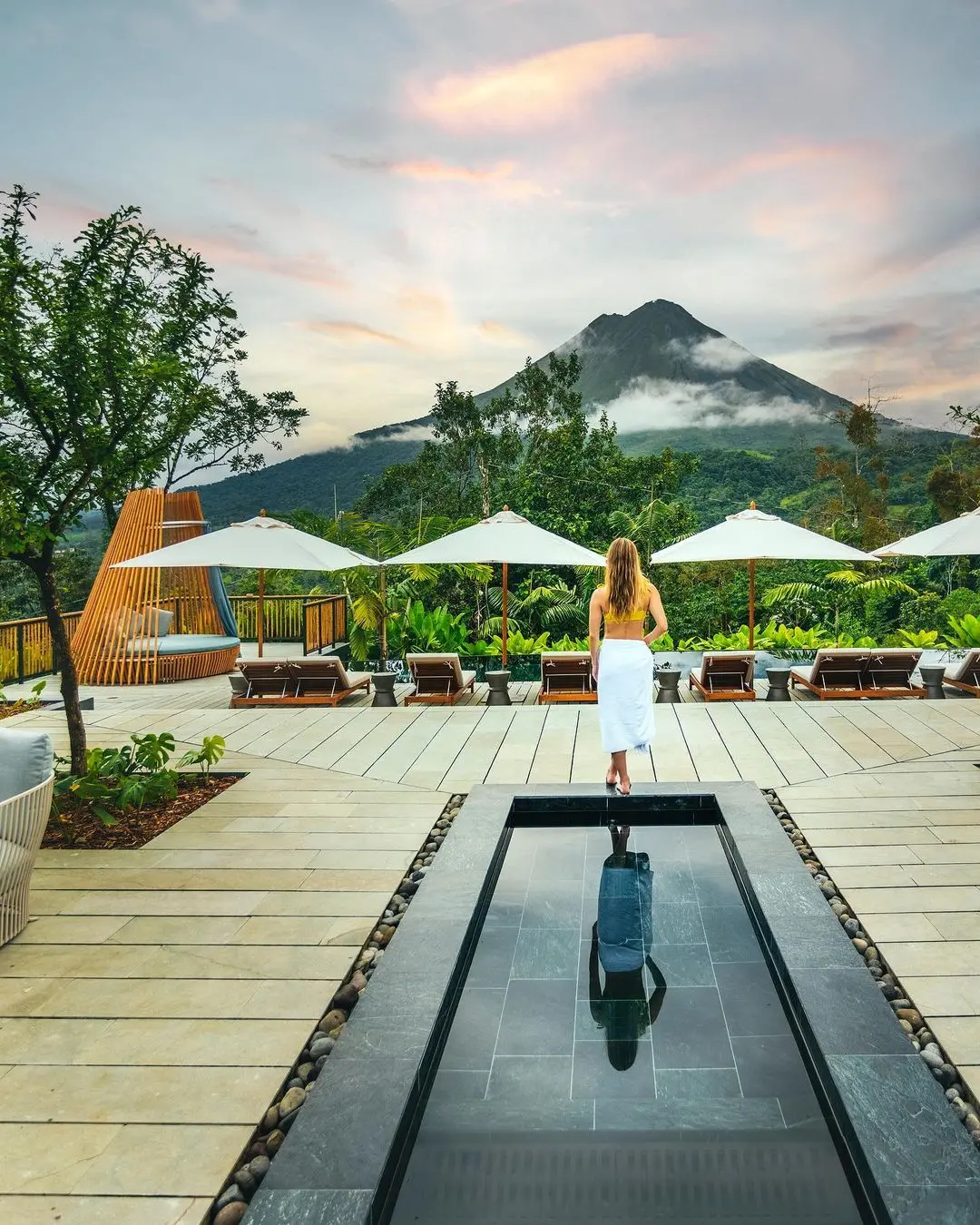A woman standing on the edge of the pool of a resort and looking at an Arenal Volcano in Costa Rica